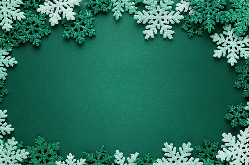 Decorative snowflakes arranged in a border around a green surface with copyspace