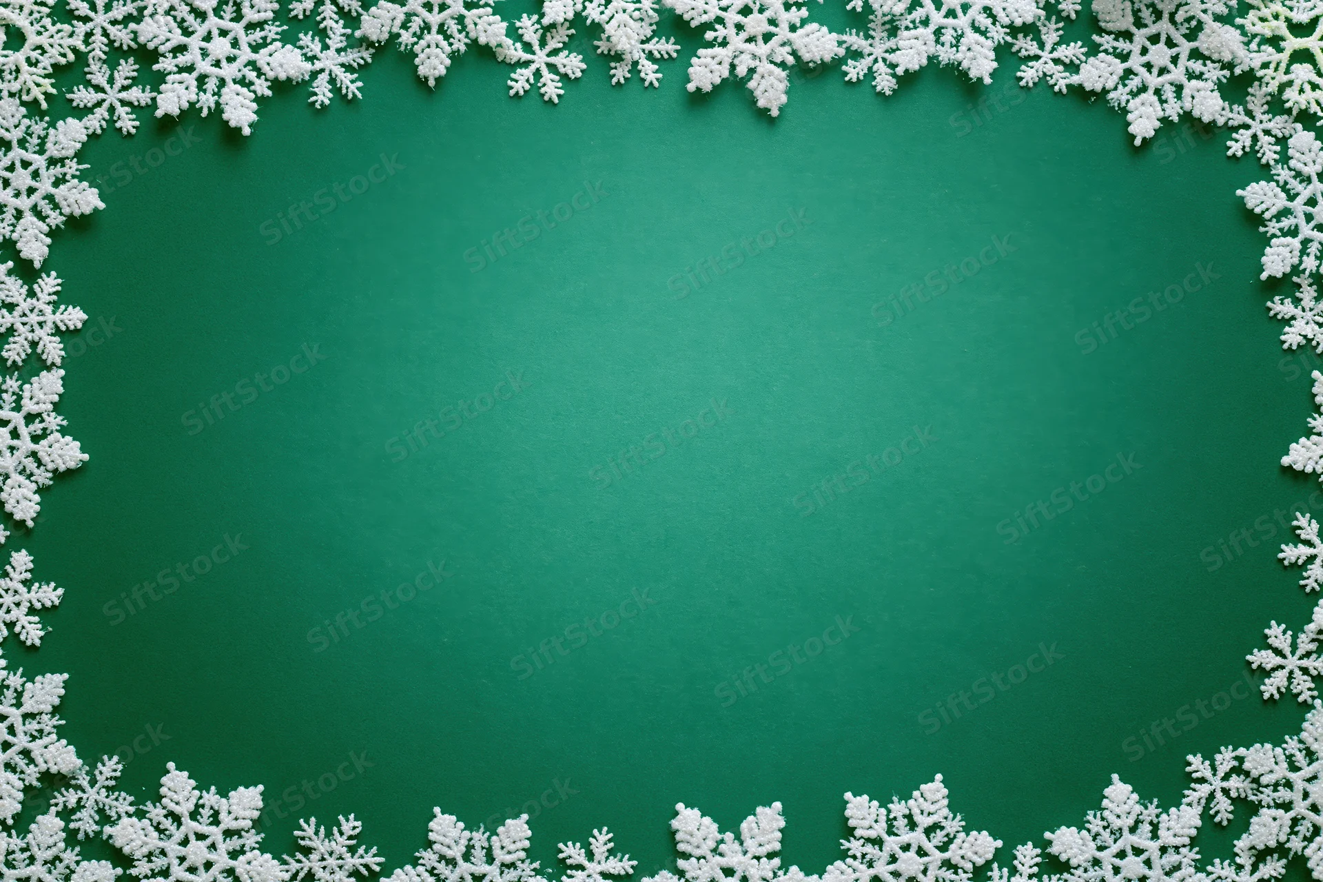 White snowflakes arranged in a border around a green flat lay background