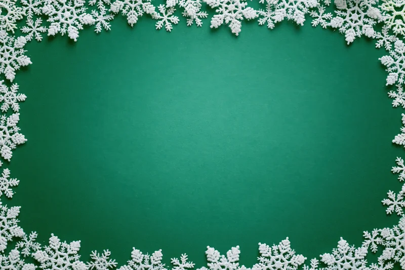 White snowflakes arranged in a border around a green flat lay background