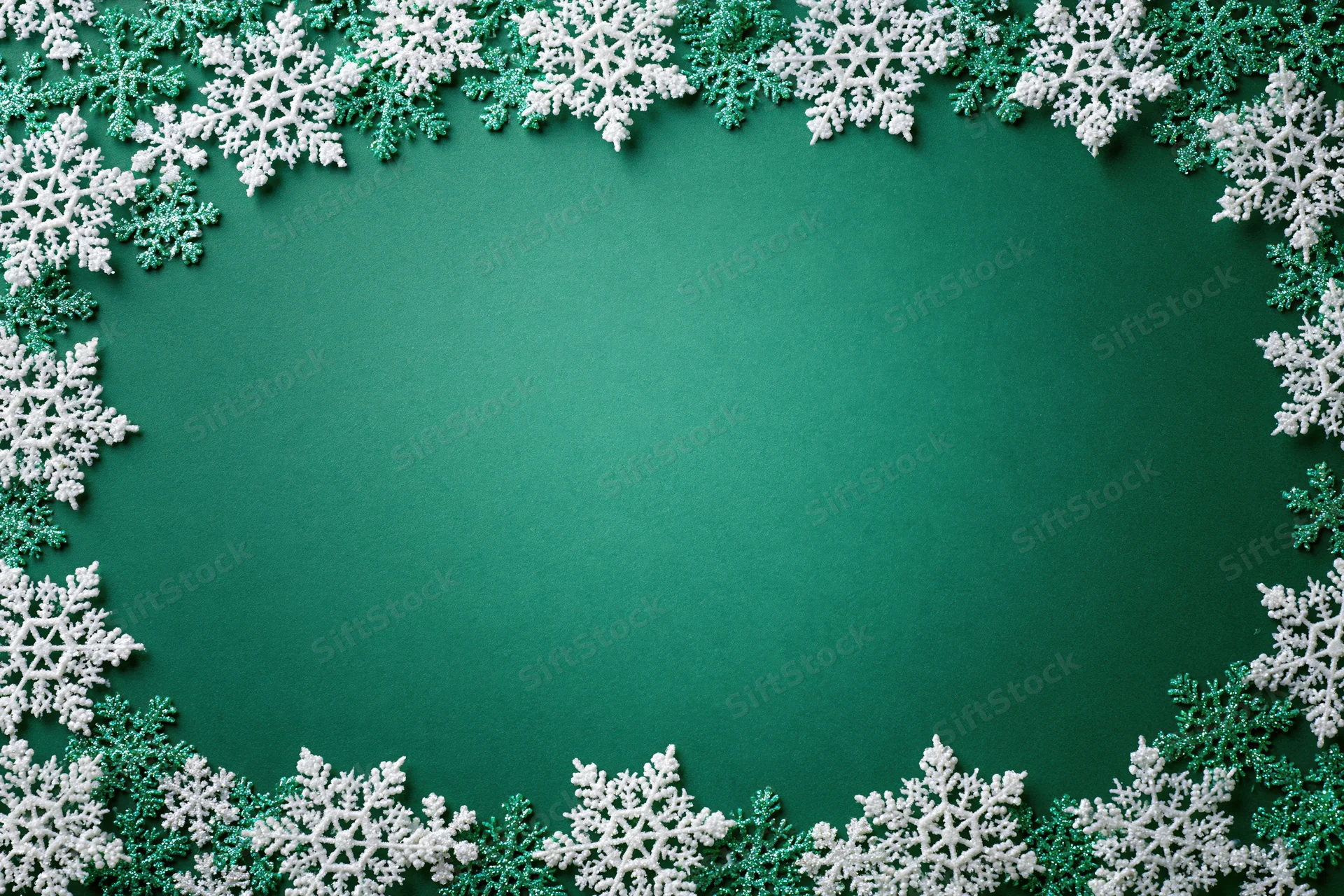 Snowflakes arranged in a border around a green surface for holiday decoration