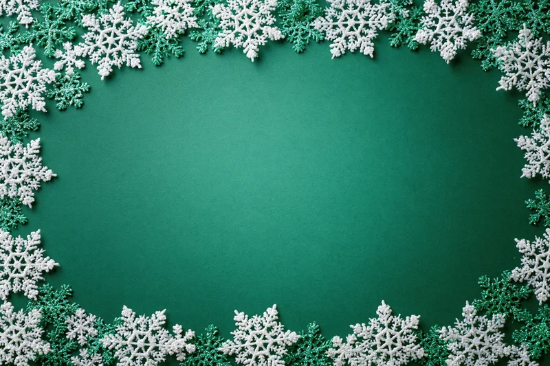 Snowflakes arranged in a border around a green surface for holiday decoration