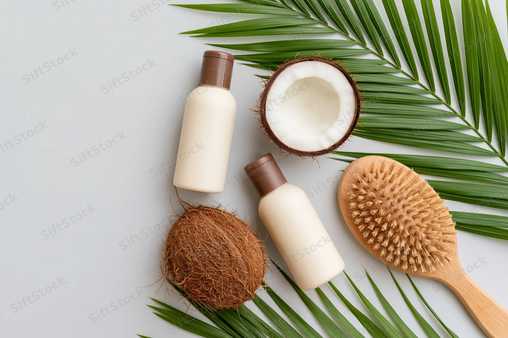 Coconut halves and haircare products arranged with palm leaves on white surface