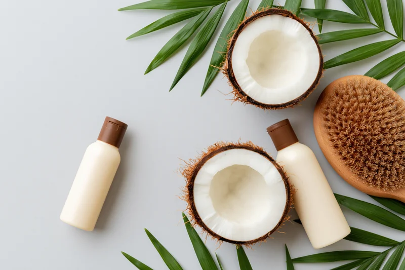 Halved coconuts and skincare bottles arranged with palm leaves on white surface