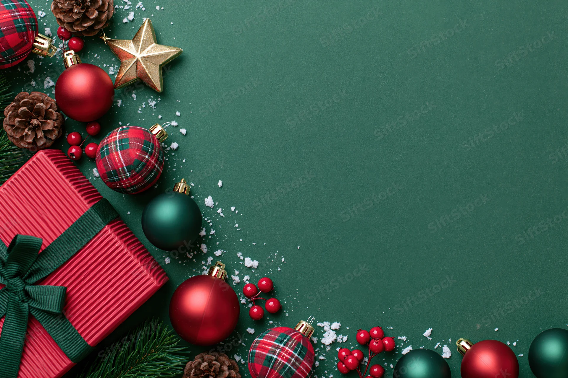 Christmas ornaments and wrapped gift arranged in flat lay on green surface with copyspace