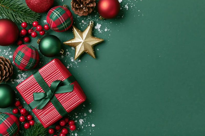 Christmas ornaments and a wrapped gift arranged on a green surface with copyspace