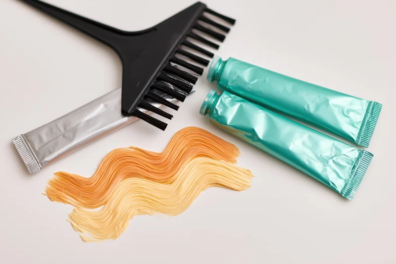 Hair dye brush and tubes with color swatch on white surface