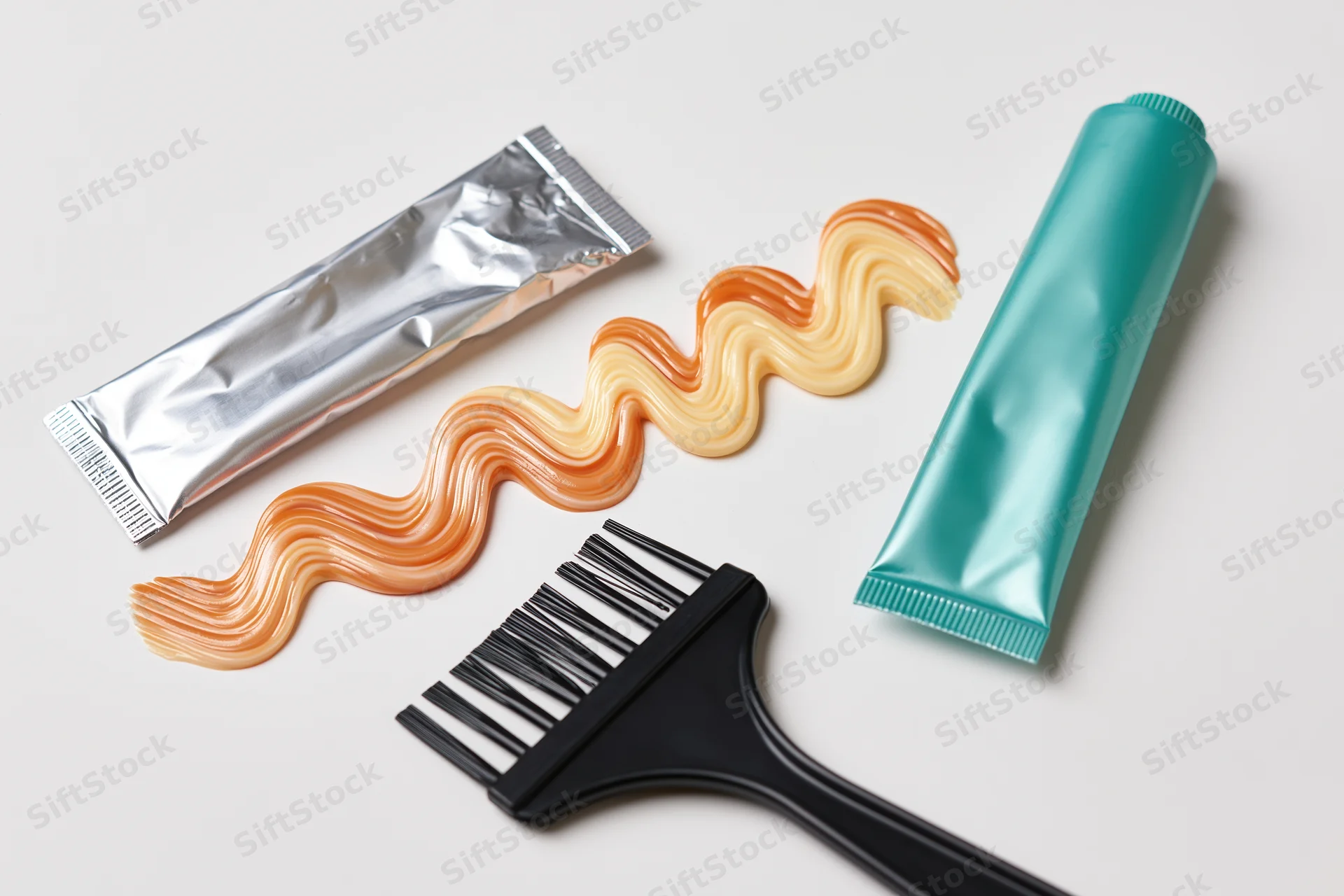 Hair dye brush and two metallic tubes with swirled dye on white surface