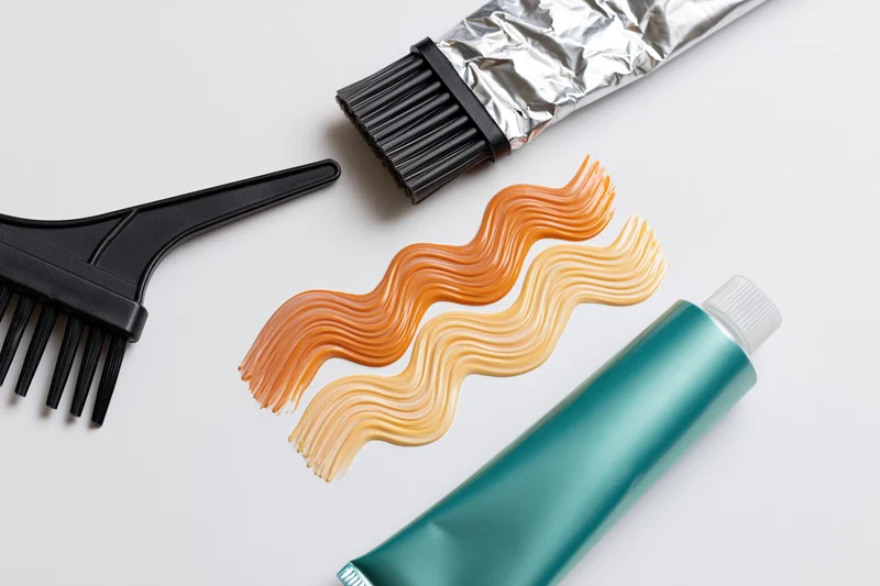 Hair dye brush and tubes with color swatches on white surface