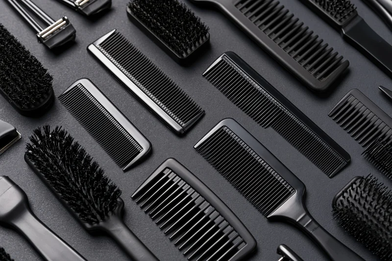Assorted black hair styling tools arranged in flat lay on dark surface