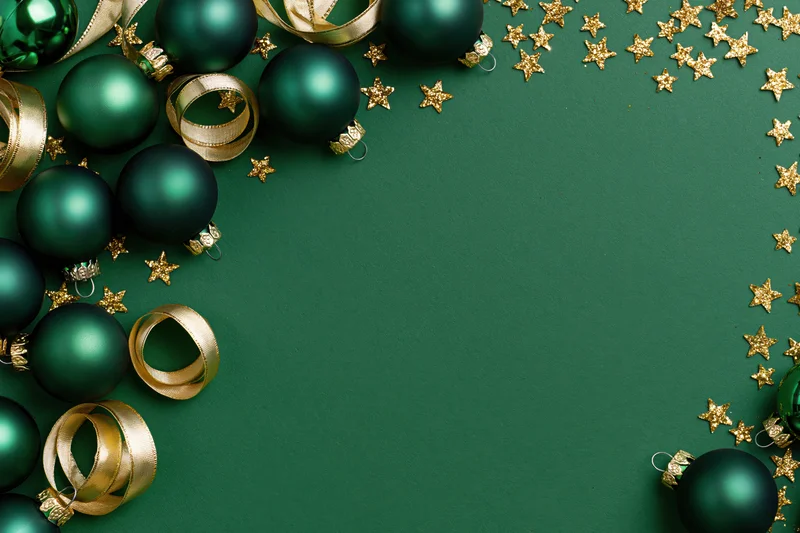 Dark green christmas ornaments and gold ribbon arranged in a border on a green surface with copyspace