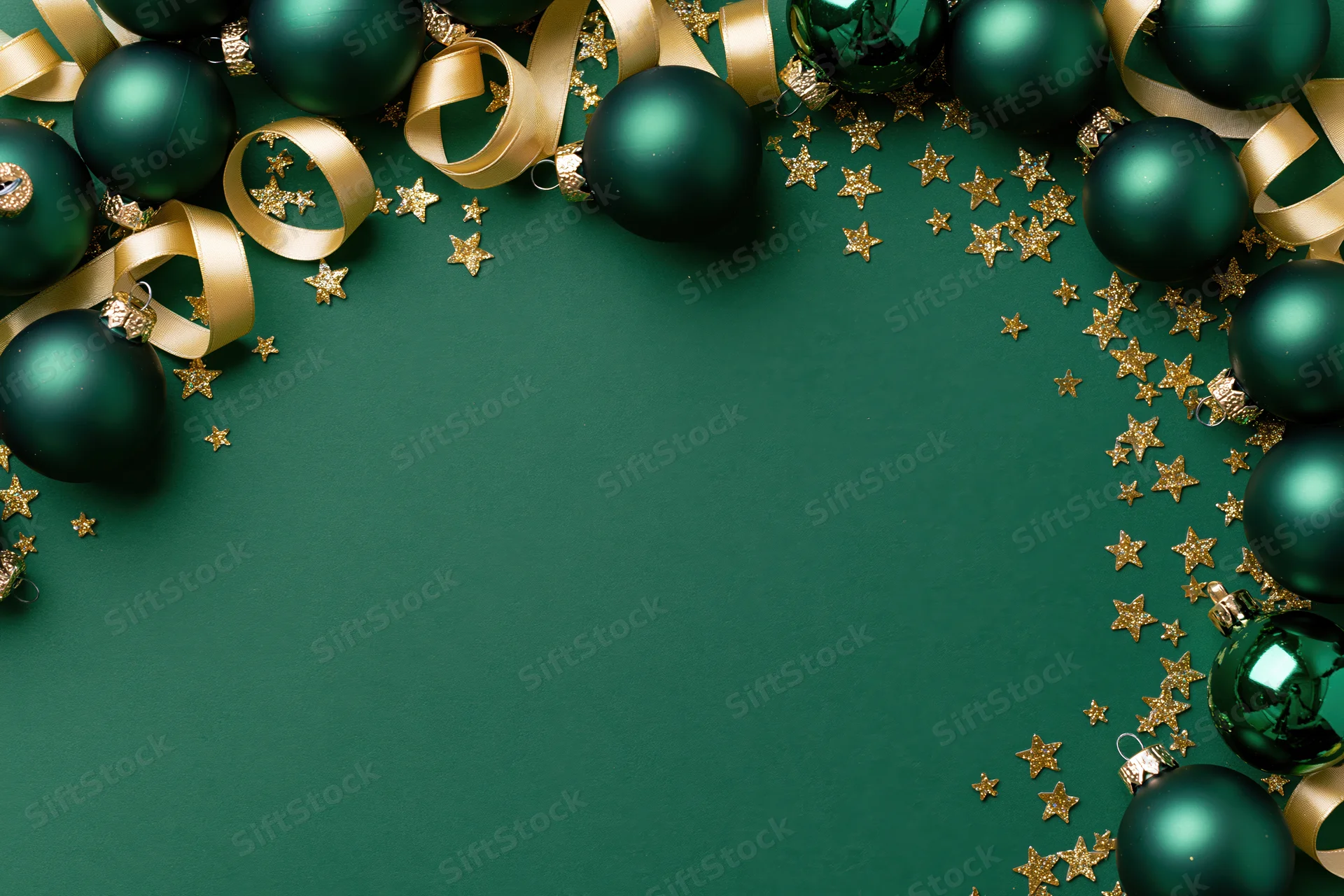 Dark green christmas ornaments and gold ribbon arranged in a frame on a green surface with copyspace