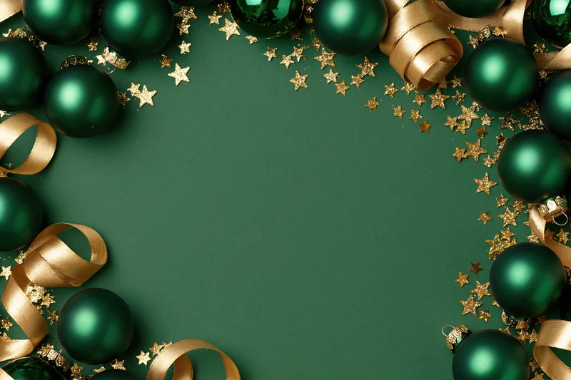Dark green christmas ornaments and gold ribbon arranged in a frame on a green surface with copyspace