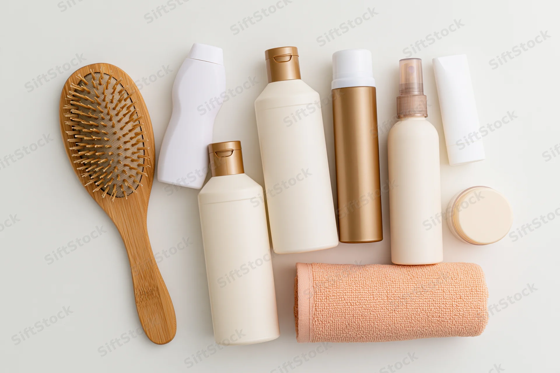 Hair care products arranged in flat lay on white surface with bamboo brush and towel