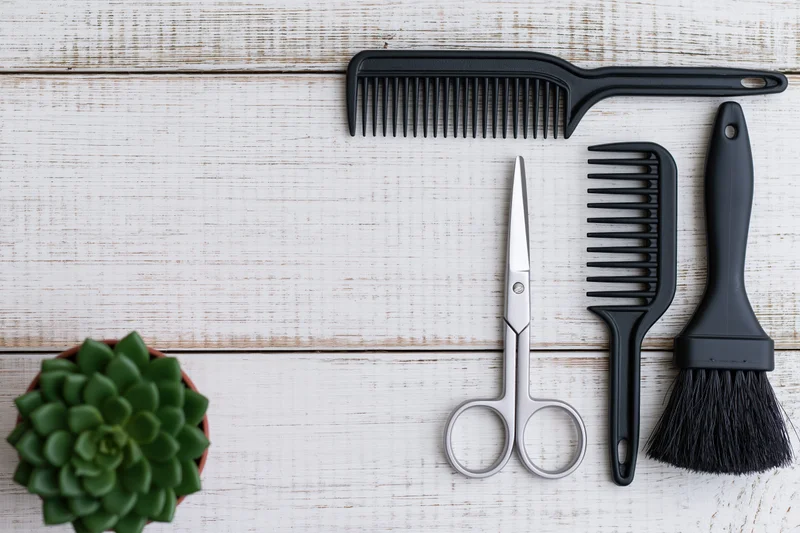 Hairdressing tools arranged on white wooden surface with succulent plant and copyspace