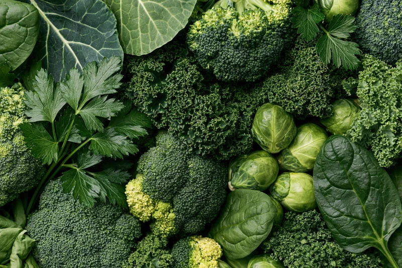 Dense flat lay of mixed green vegetables including broccoli, kale, spinach, brussels sprouts, and parsley arranged to fill the frame