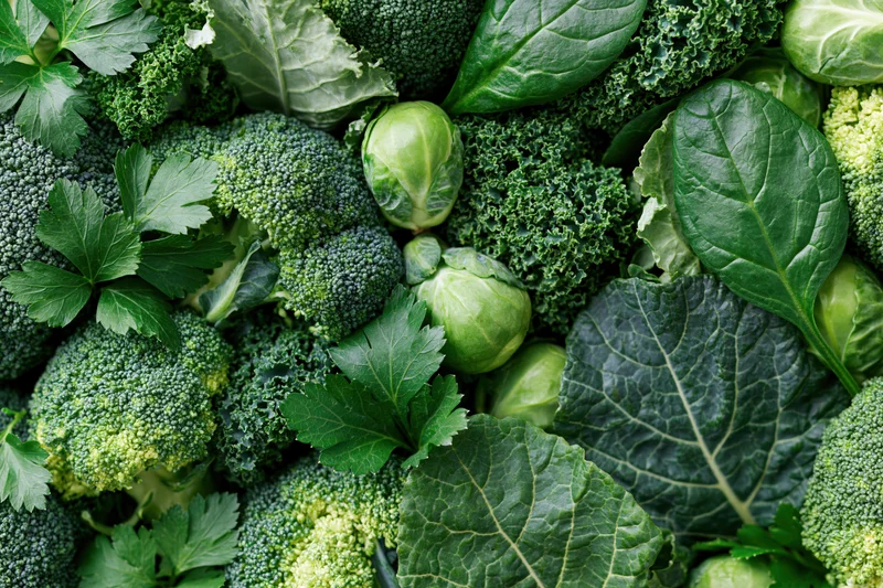 Dense flat lay of mixed green vegetables including broccoli kale brussels sprouts and parsley arranged to fill the frame