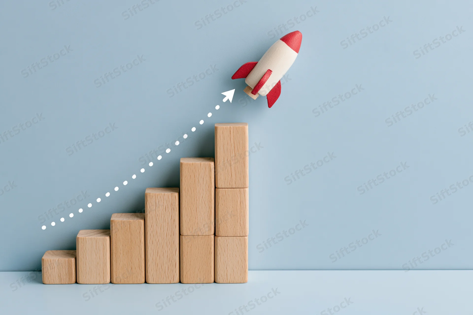 Wooden blocks arranged in ascending bar chart with toy rocket launching upward along dotted path