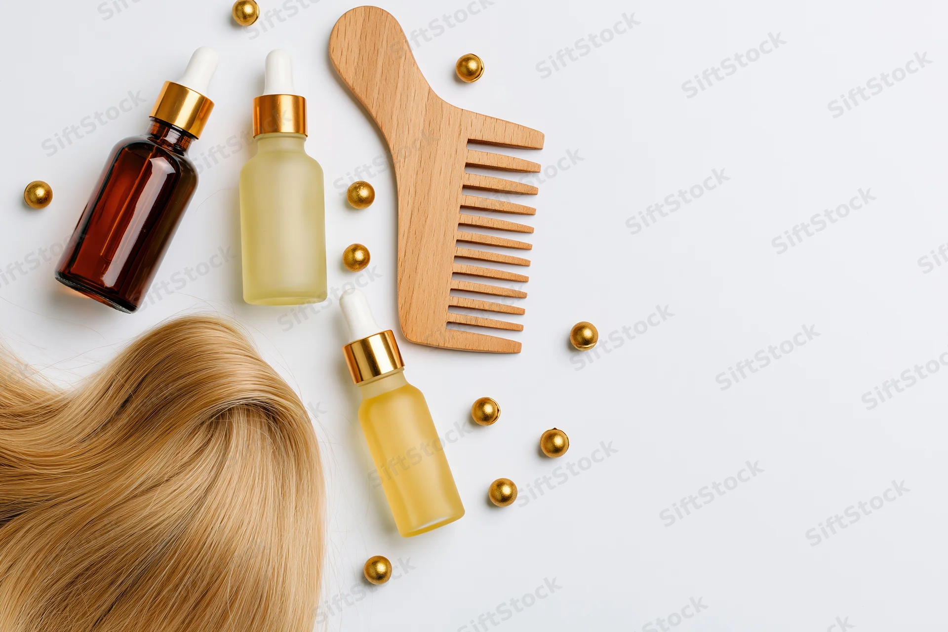 Blonde hair strand curled with haircare products and wooden comb on white surface