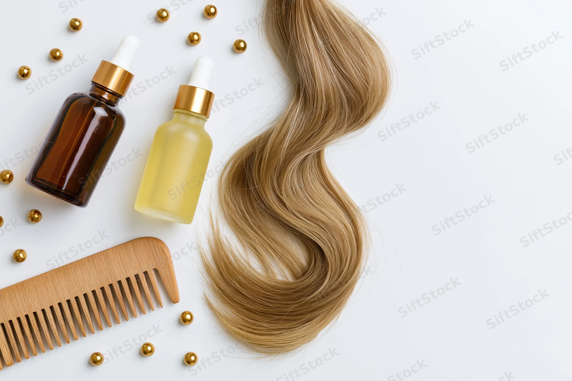 Blonde hair strand curled in a wave with haircare products and a wooden comb on a white surface