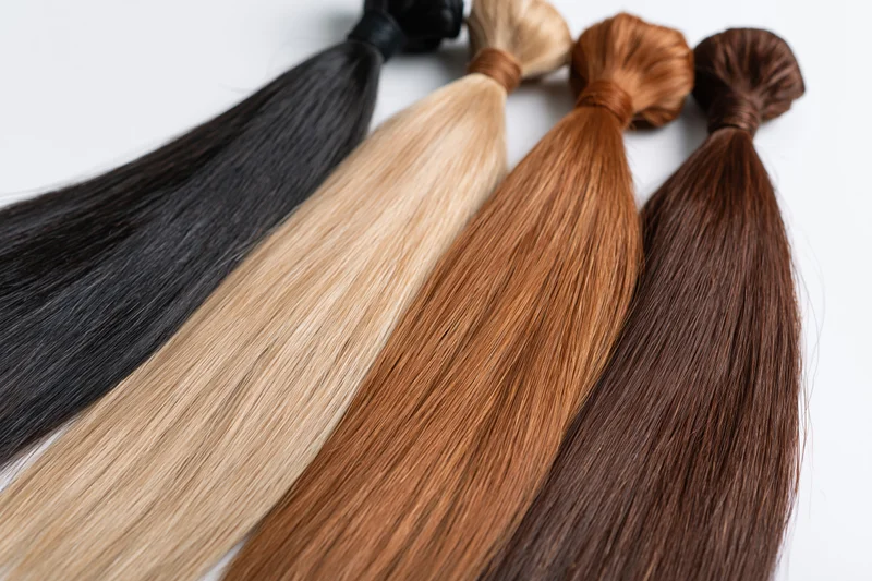 Four bundles of hair extensions in black, blonde, auburn and brown arranged on white background