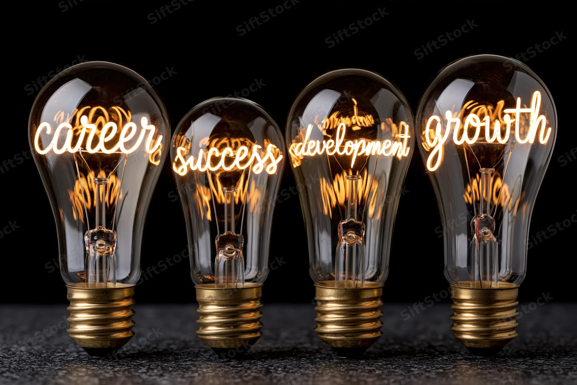 Four glowing incandescent lightbulbs in a row displaying the words career, success, development, and growth against a black background