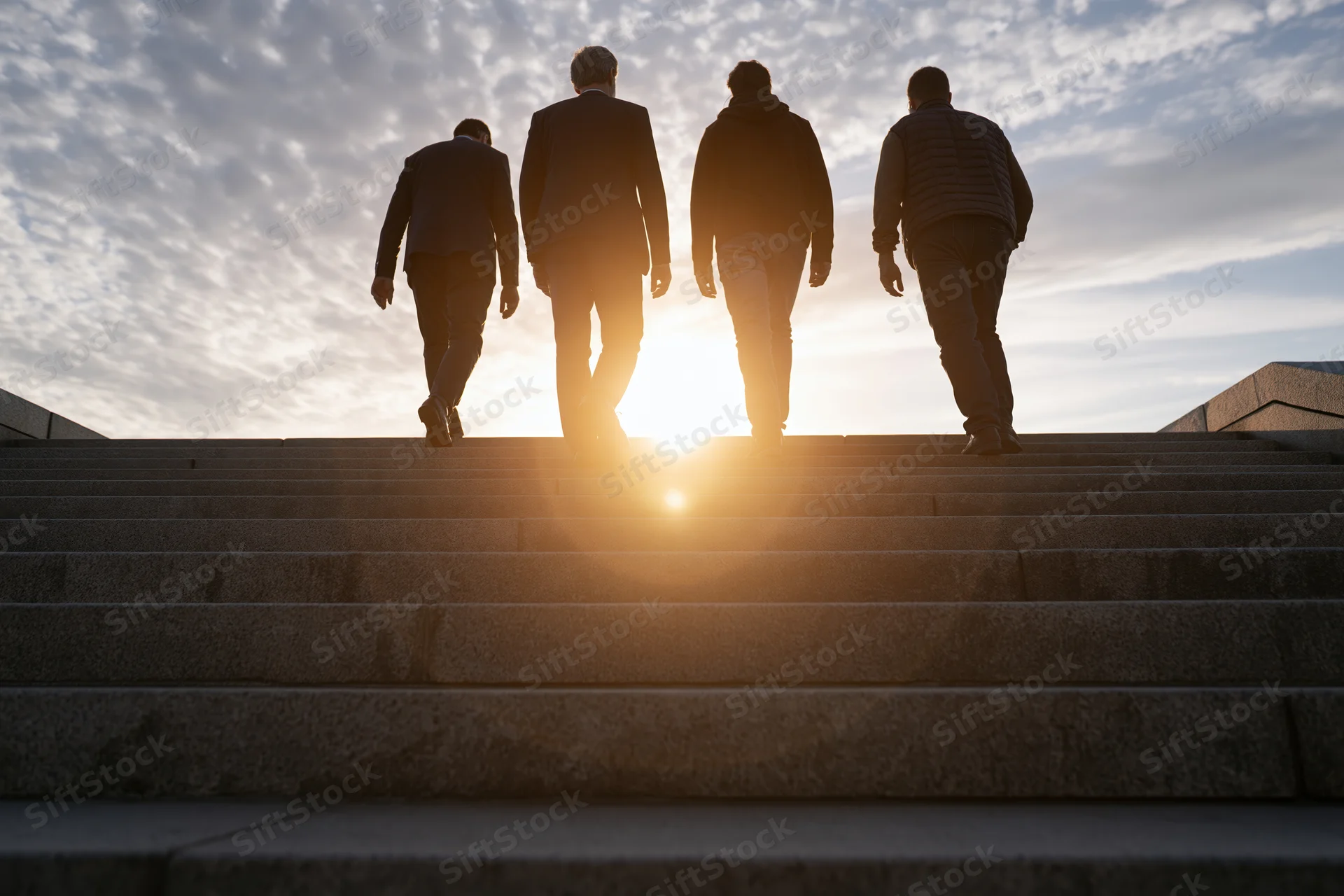 Four men walking up wide granite stairs at sunset, silhouetted against the sky