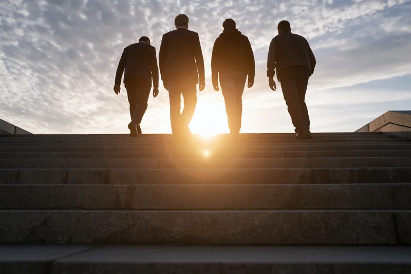 Four men walking up wide granite stairs at sunset, silhouetted against the sky