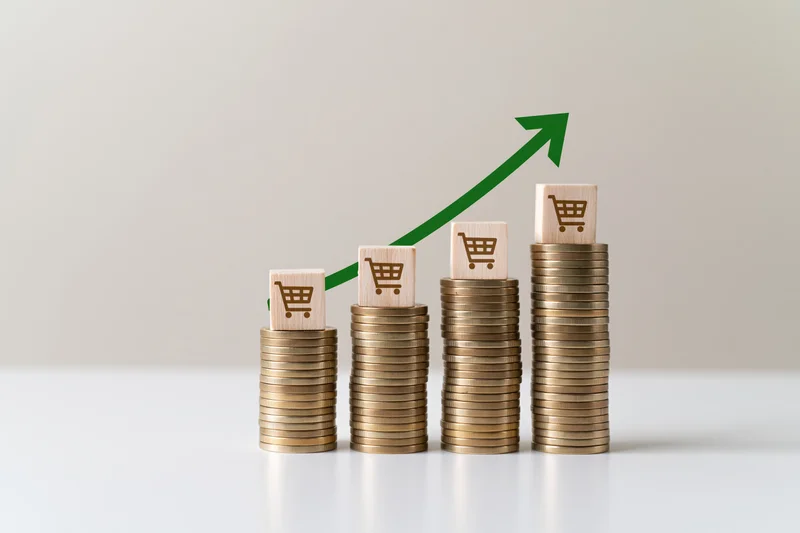 Stacks of coins increasing in height with shopping cart icons and green arrow indicating growth in e-commerce sales