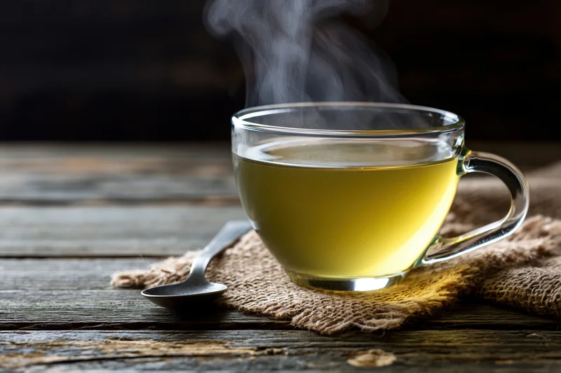 Steaming green tea in a glass cup on burlap cloth over wooden table