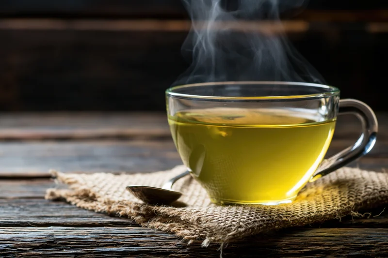 Steaming green tea in a glass cup on burlap cloth over wooden table