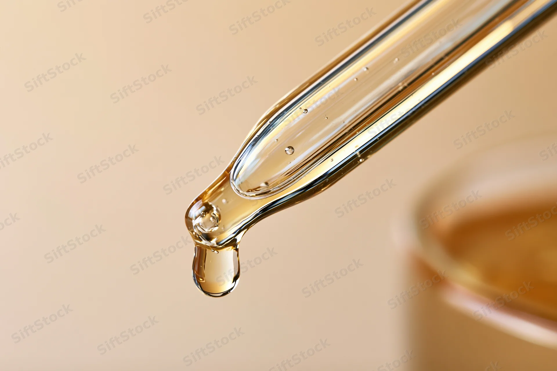Glass pipette dropper releasing a golden serum drop against a neutral background