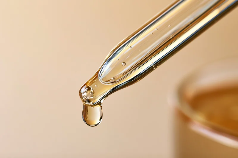 Glass pipette dropper releasing a golden serum drop against a neutral background