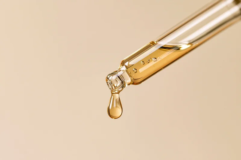 Glass pipette dropper releasing a golden serum drop against a neutral background