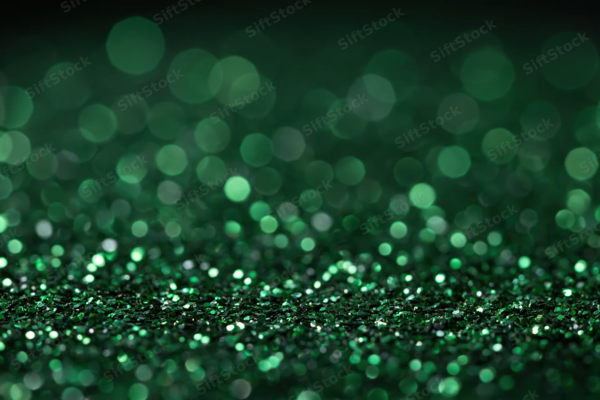 Green glitter particles scattered across a black surface with bokeh effect