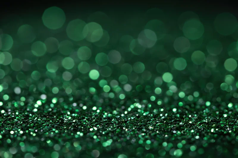 Green glitter particles scattered across a black surface with bokeh effect