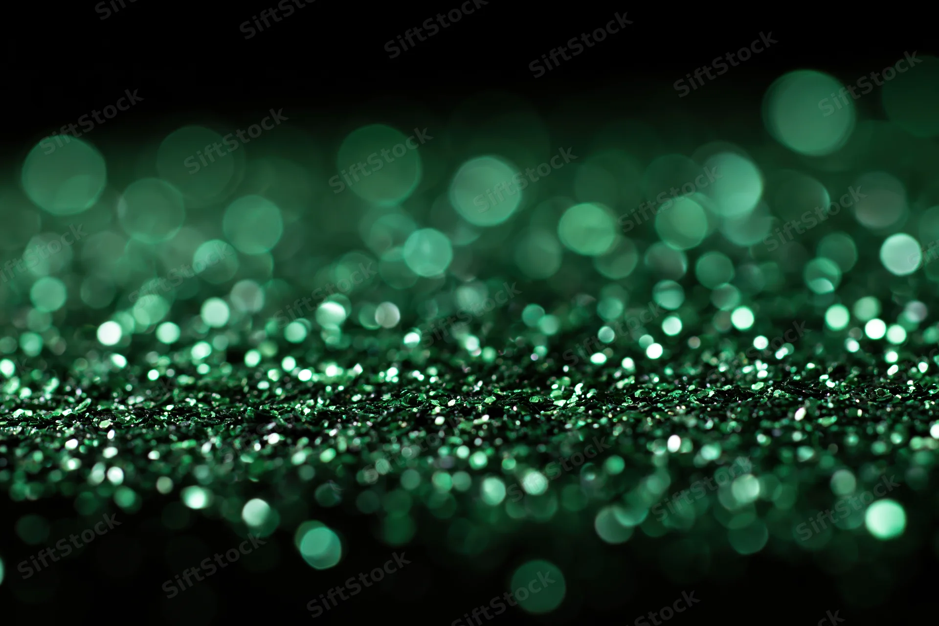 Green glitter particles scattered across a flat black surface with bokeh effect