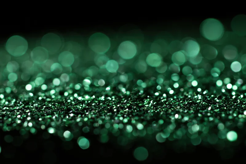 Green glitter particles scattered across a flat black surface with bokeh effect