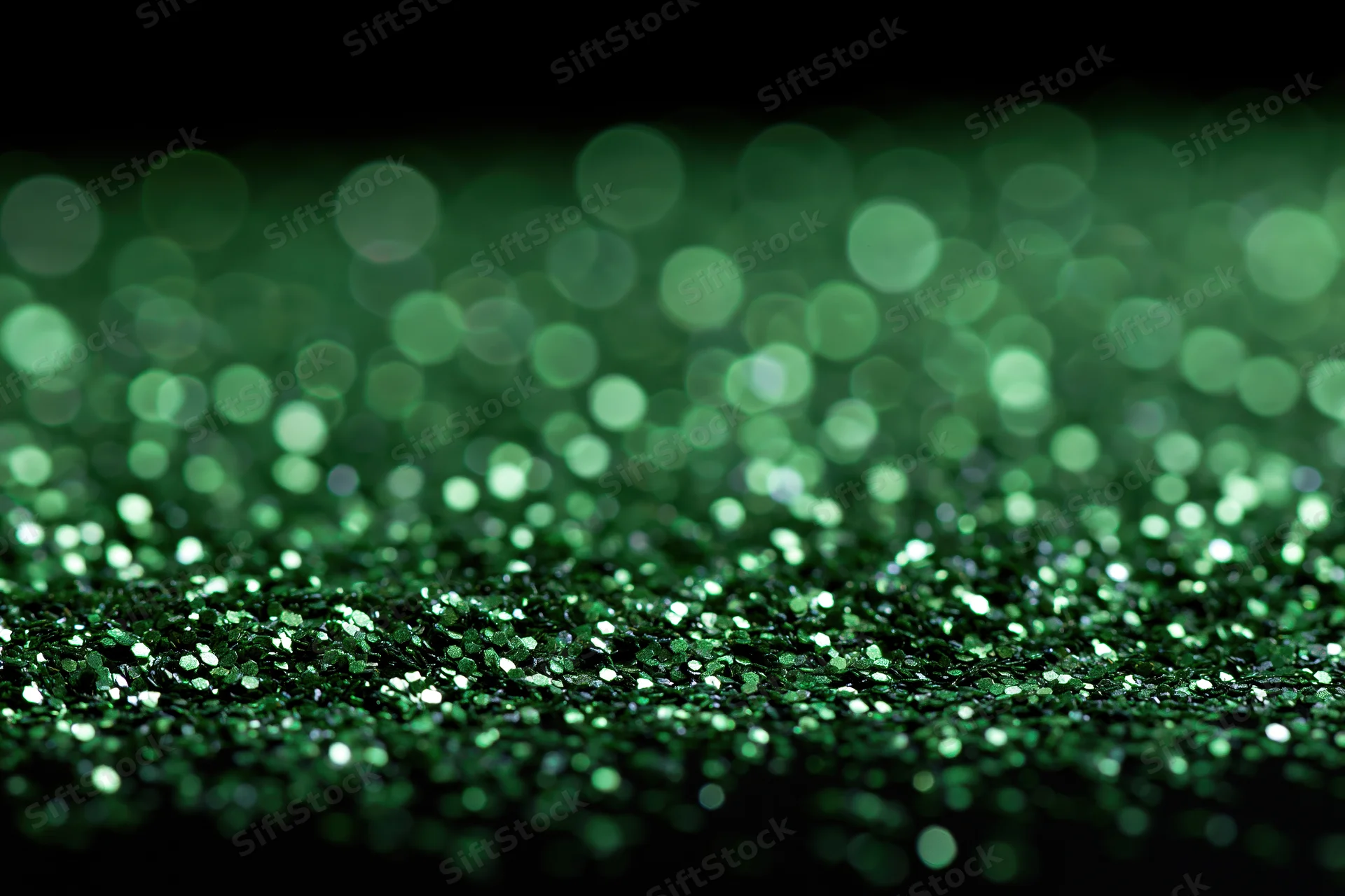 Green glitter scattered across a black surface with bokeh lights in the background