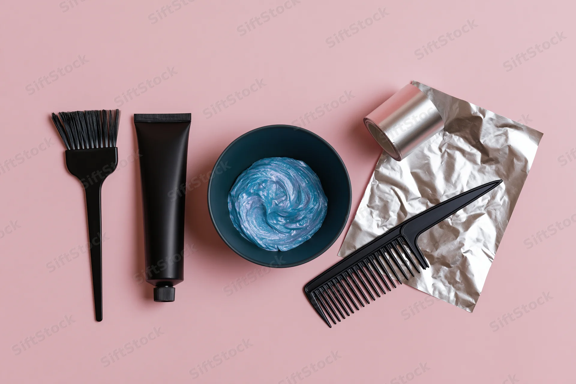 Hair coloring tools arranged in flat lay on pink surface