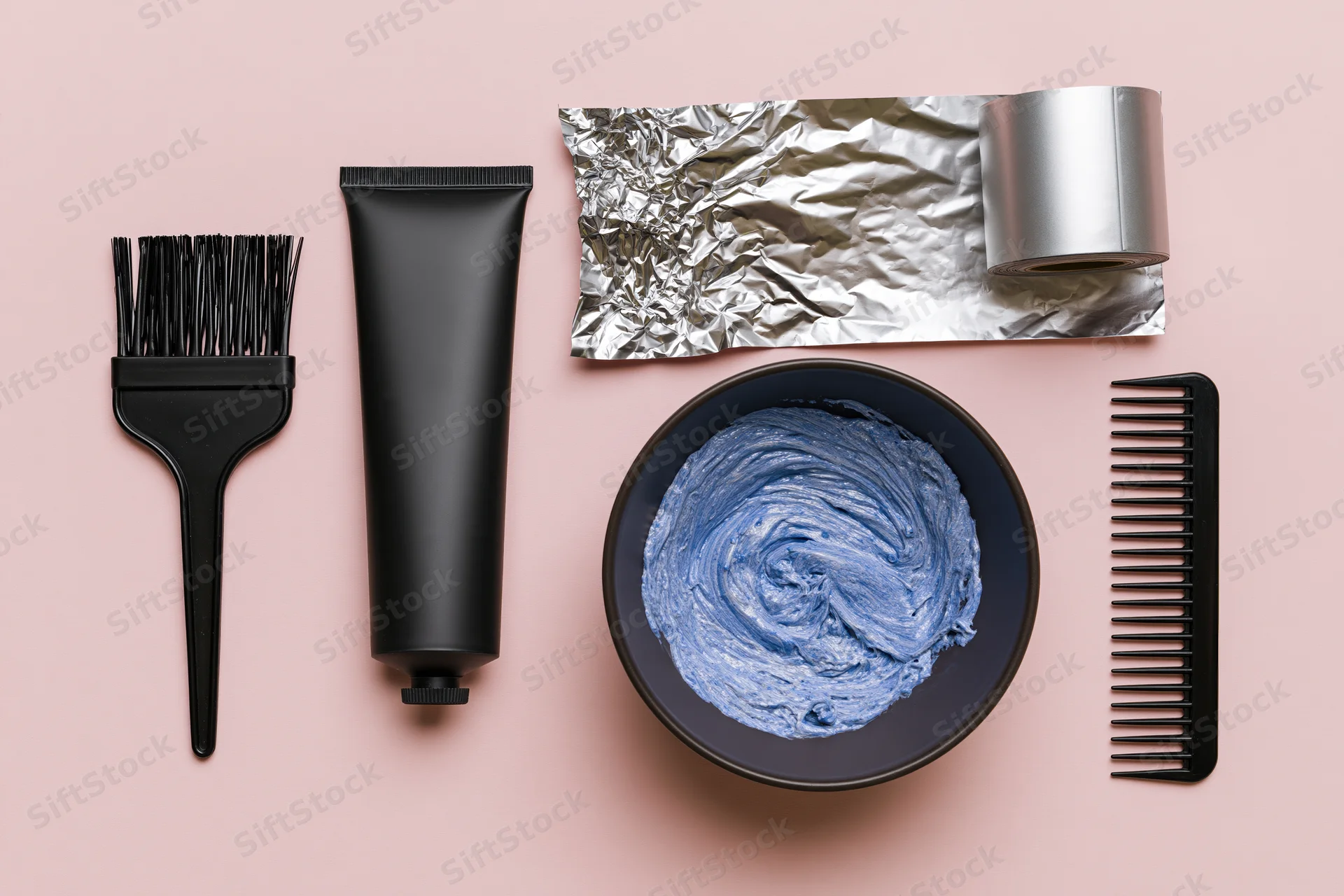 Hair coloring tools arranged in flat lay on pink background with copyspace