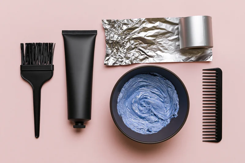 Hair coloring tools arranged in flat lay on pink background with copyspace