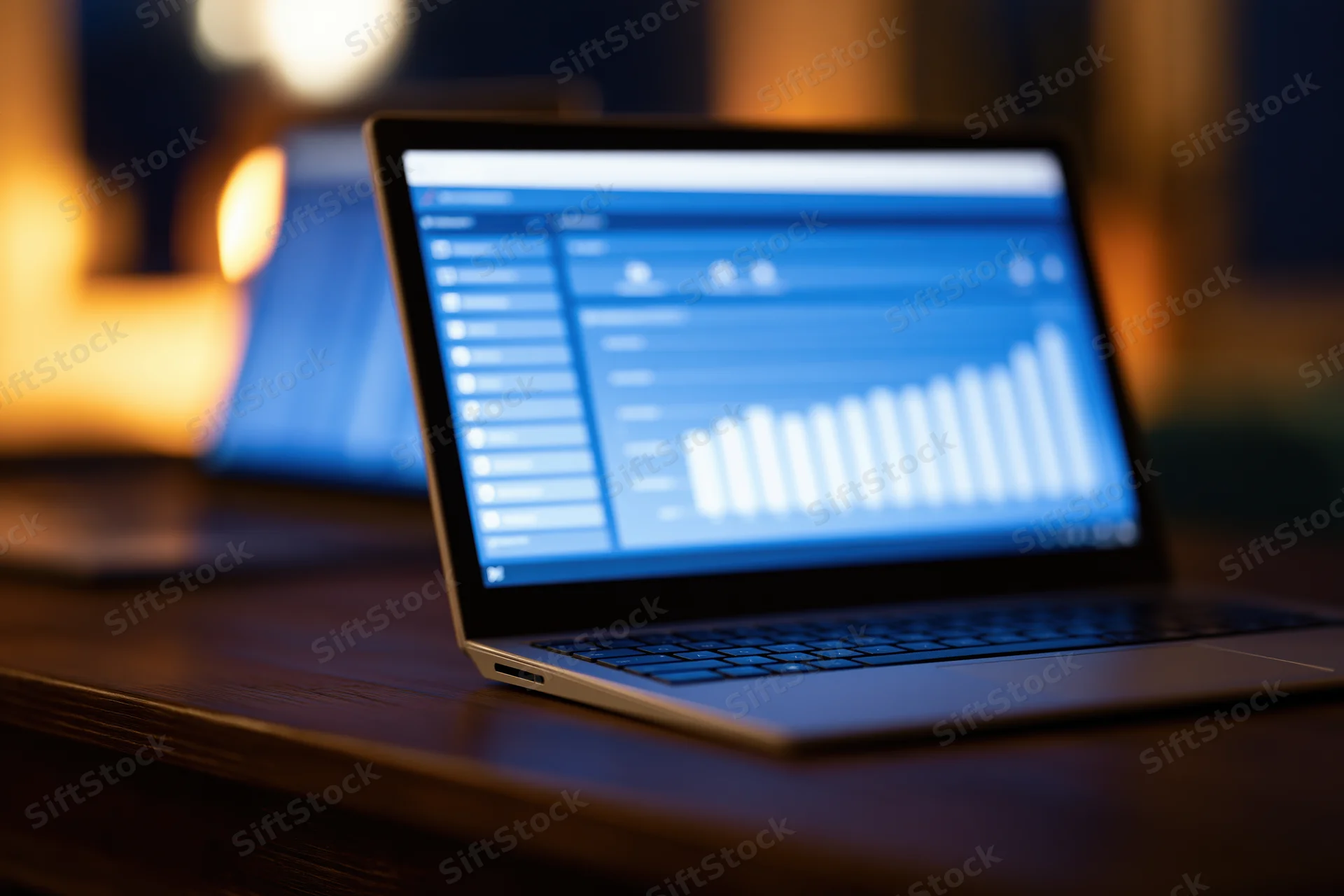 Laptop displaying data dashboard with bar chart on dark wooden desk at night