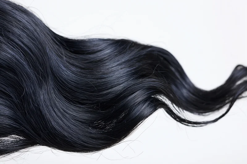 Long black wavy hair extension floating midair against white background