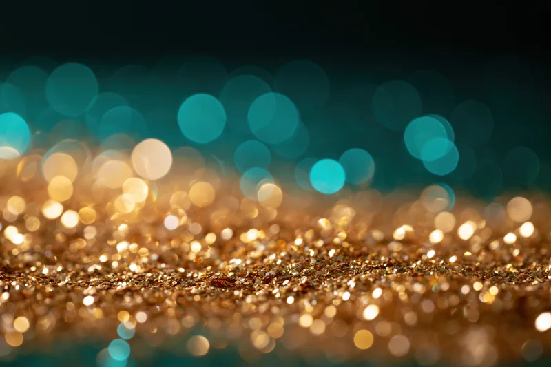 Gold glitter scattered on dark surface with teal bokeh lights in background