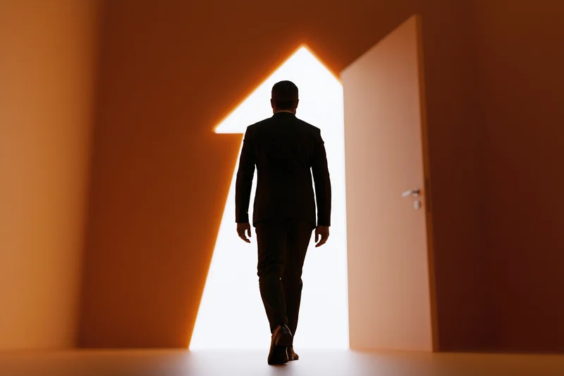 Man in dark suit walking toward glowing doorway in dim interior