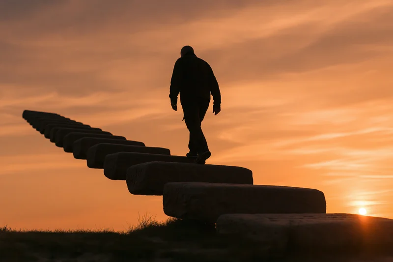 Man walking upward on stone steps against a warm sunset sky