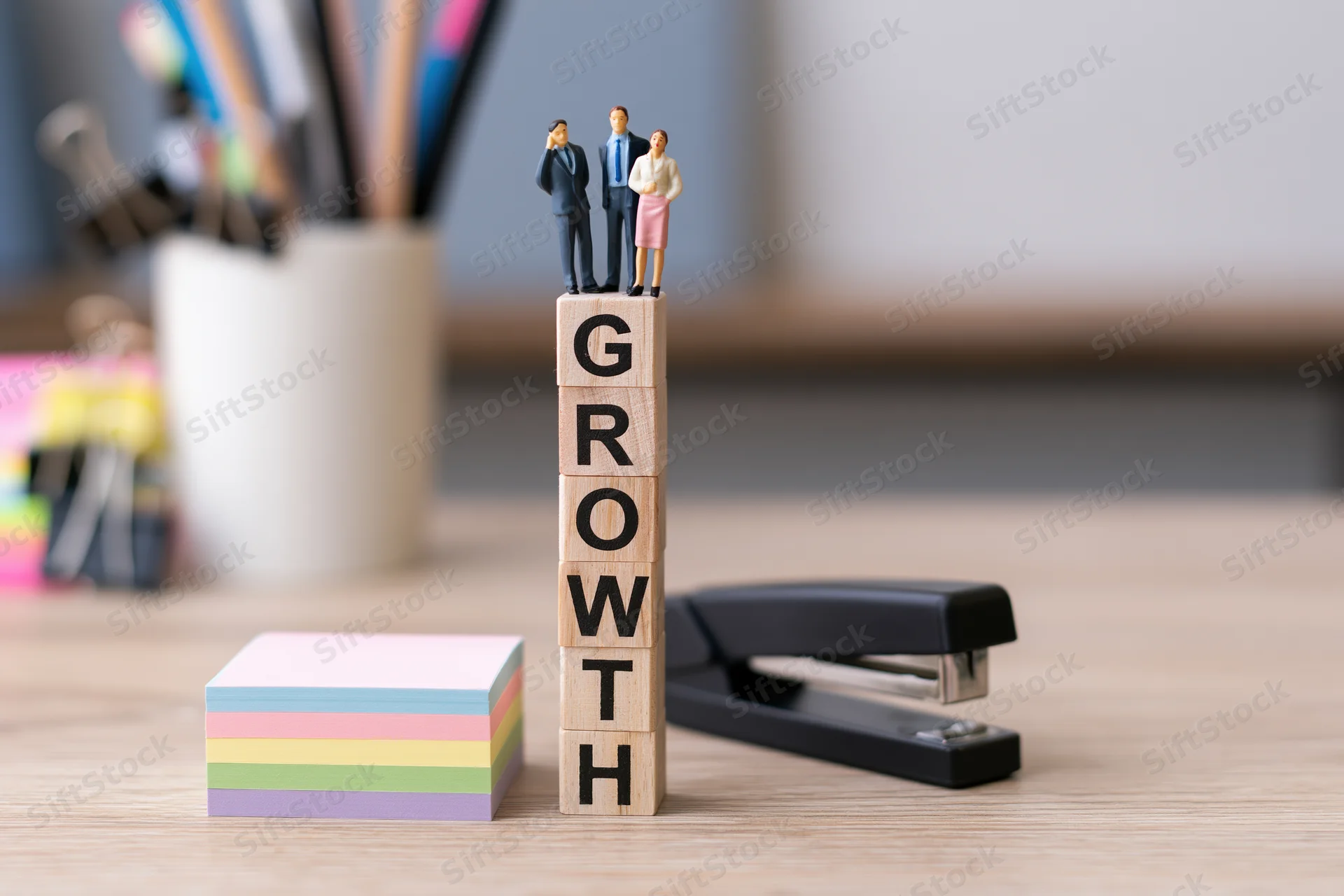 Miniature businesspeople standing on stacked wooden blocks spelling growth on an office desk