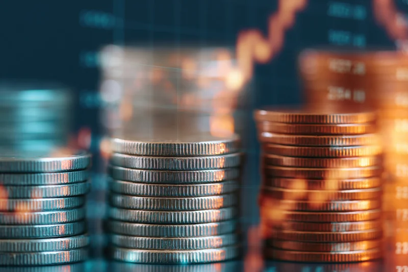 Stacks of silver and copper coins arranged in columns with financial graph overlay