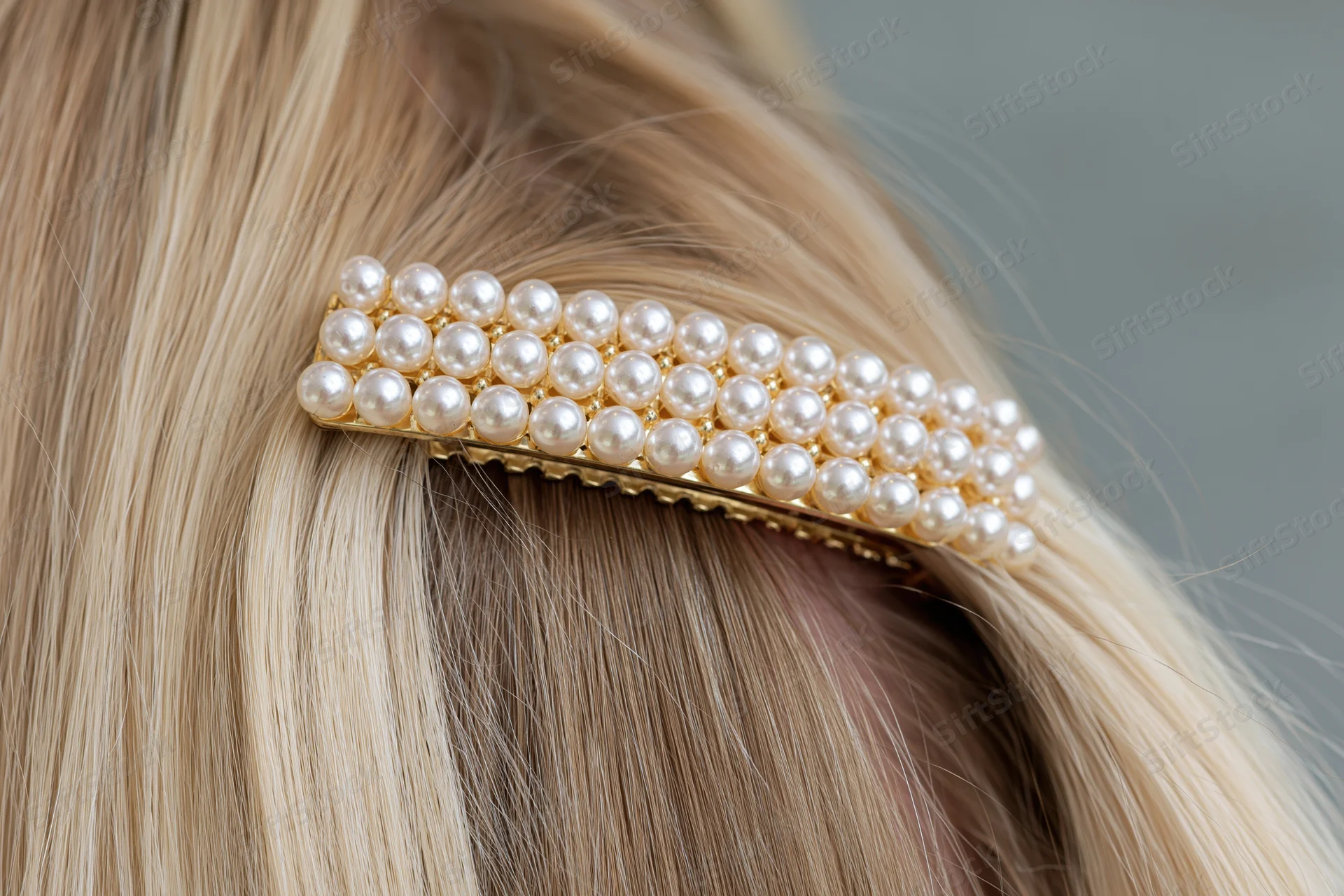 Gold pearl-studded hairclip securing a section of blonde hair