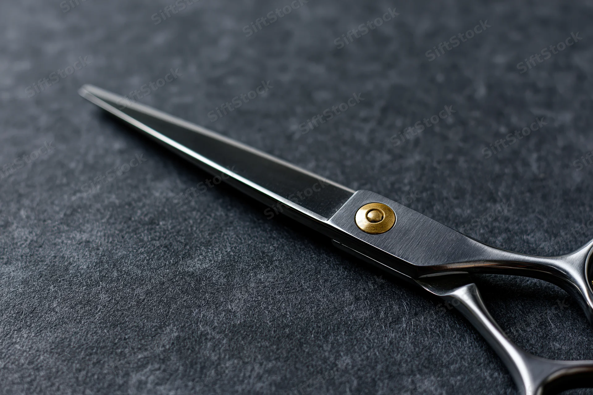 Barber scissors lying open on a dark textured surface